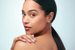 Woman with dark hair and firm skin looks over her shoulder at the camera on a blue background.